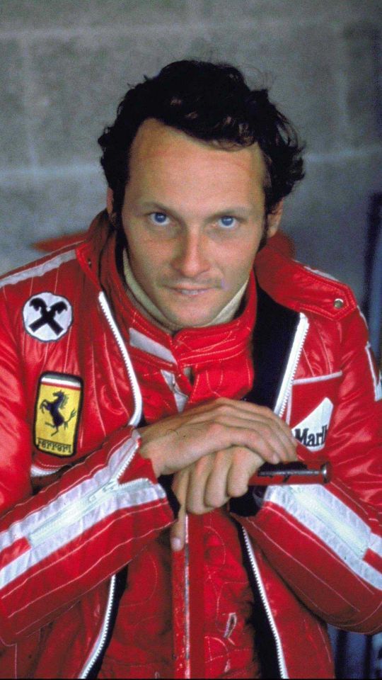 a man in a red racing suit with his hands on his hips and looking at the camera