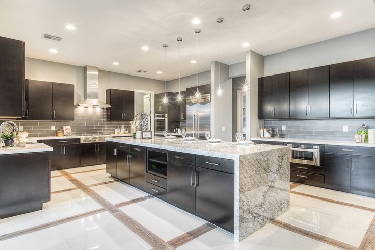 a large kitchen with marble counter tops and black cabinets, along with stainless steel appliances