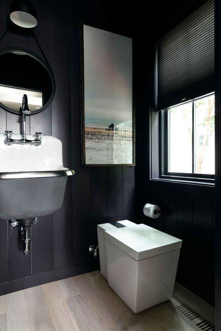 a white toilet sitting next to a bathroom sink under a mirror in a black room