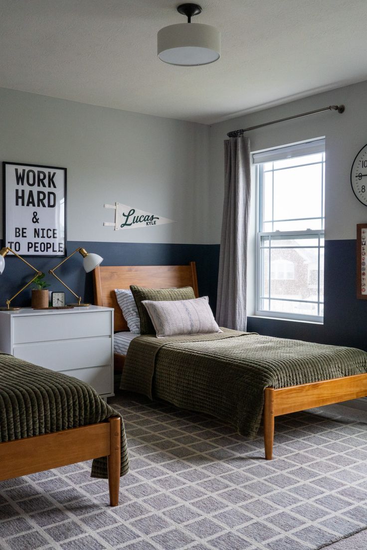 two beds in a bedroom with blue walls and carpeted flooring next to windows