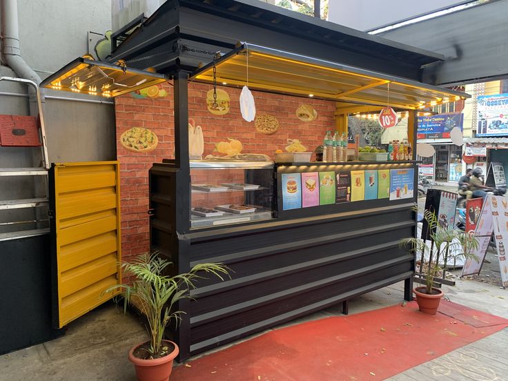 a food stand with lots of items on display in front of the counter and potted plants next to it