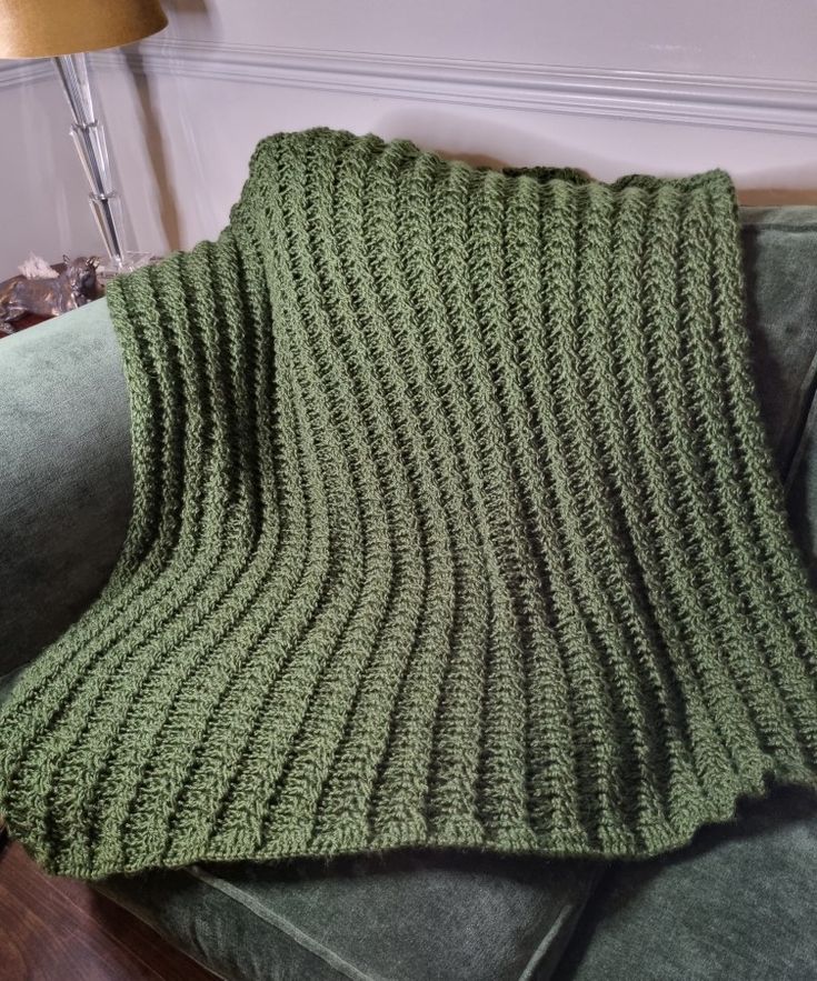 a green knitted blanket sitting on top of a couch