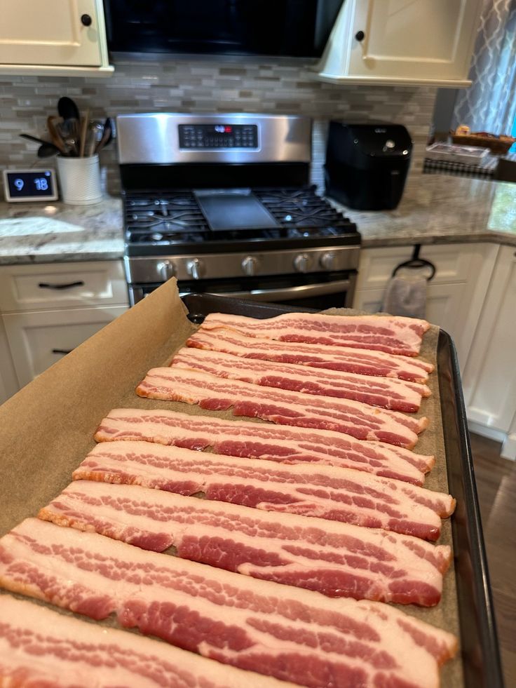 bacon strips are lined up on a baking sheet in the kitchen, ready to go into the oven