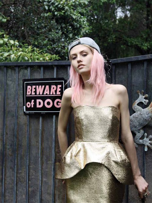 a woman with pink hair is standing in front of a fence wearing a gold dress