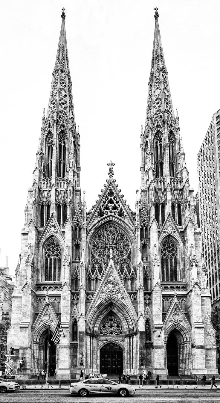 a black and white photo of a cathedral with cars parked in the street below it