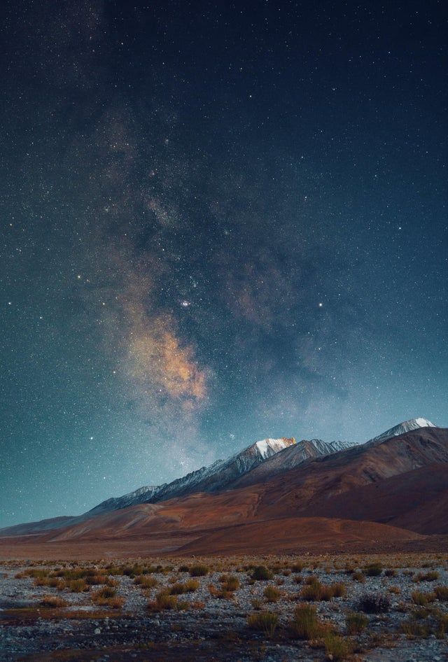 the night sky is filled with stars and clouds above a mountain range in the desert