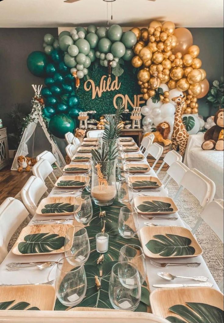 a table set up for a jungle themed birthday party with gold, green and white balloons