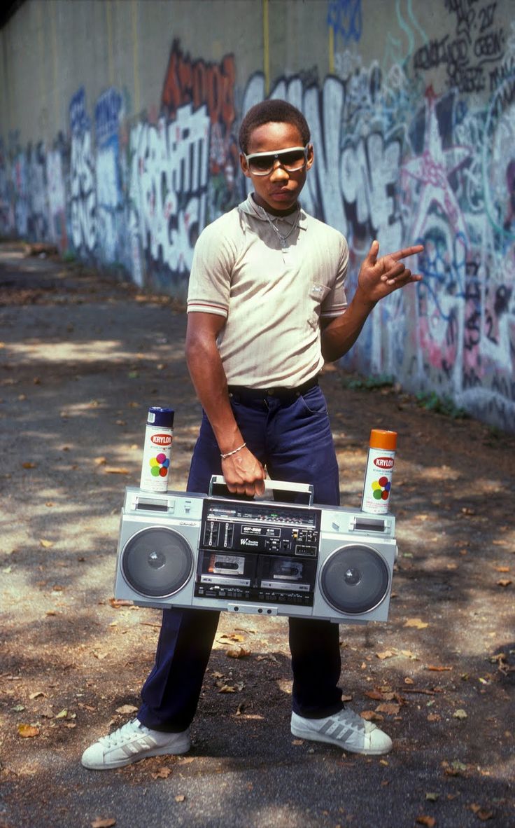 a man standing in front of a wall with graffiti on it holding a boombox