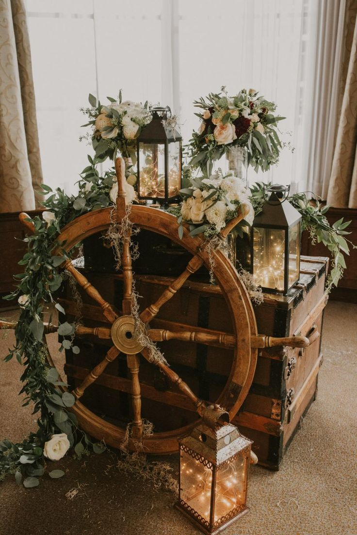 a wooden wheel decorated with flowers and greenery on the floor next to a window