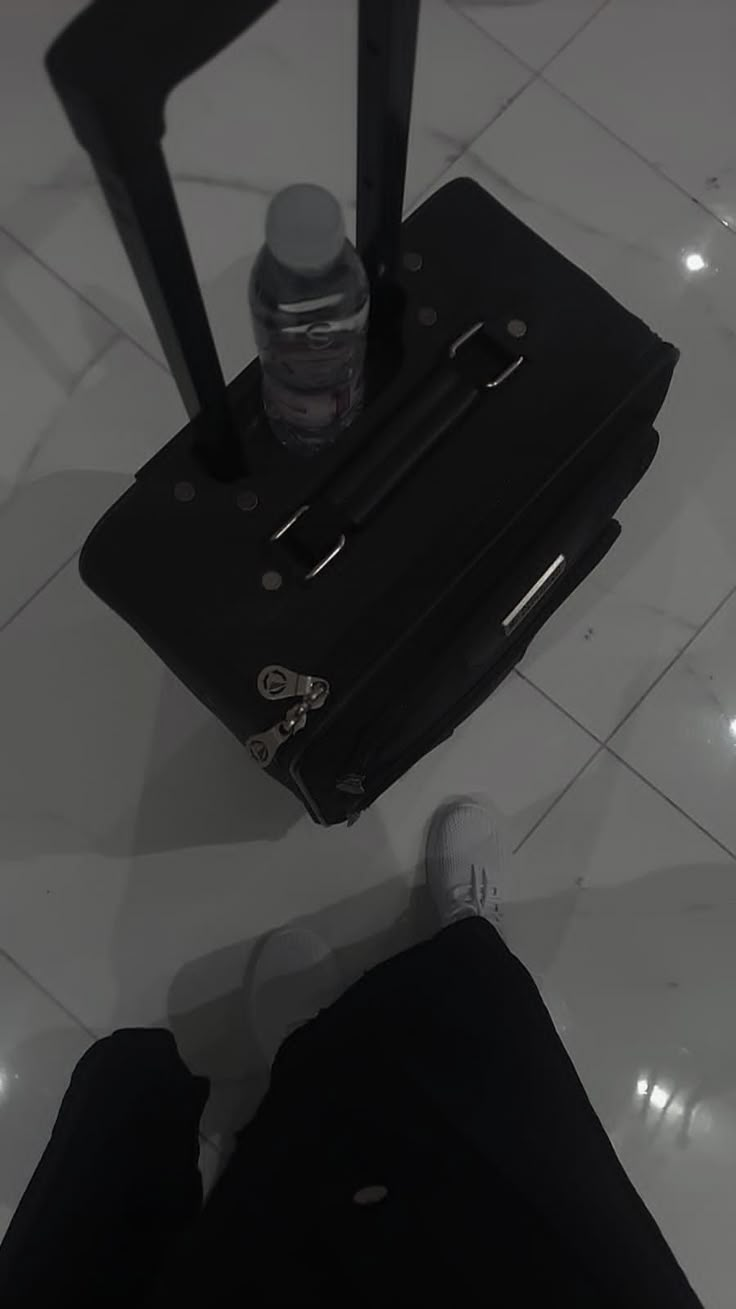 a black piece of luggage sitting on top of a white floor next to a person's feet