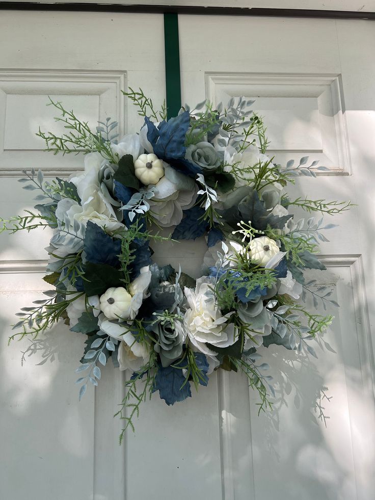 a wreath on the front door with flowers and greenery hanging from it's side