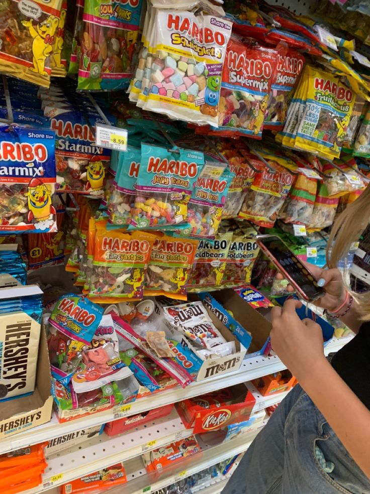 a woman is looking at her cell phone in front of a store filled with snacks