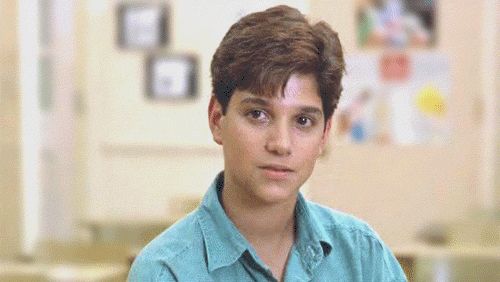 a boy in a blue shirt is sitting down and looking at the camera with serious expression on his face