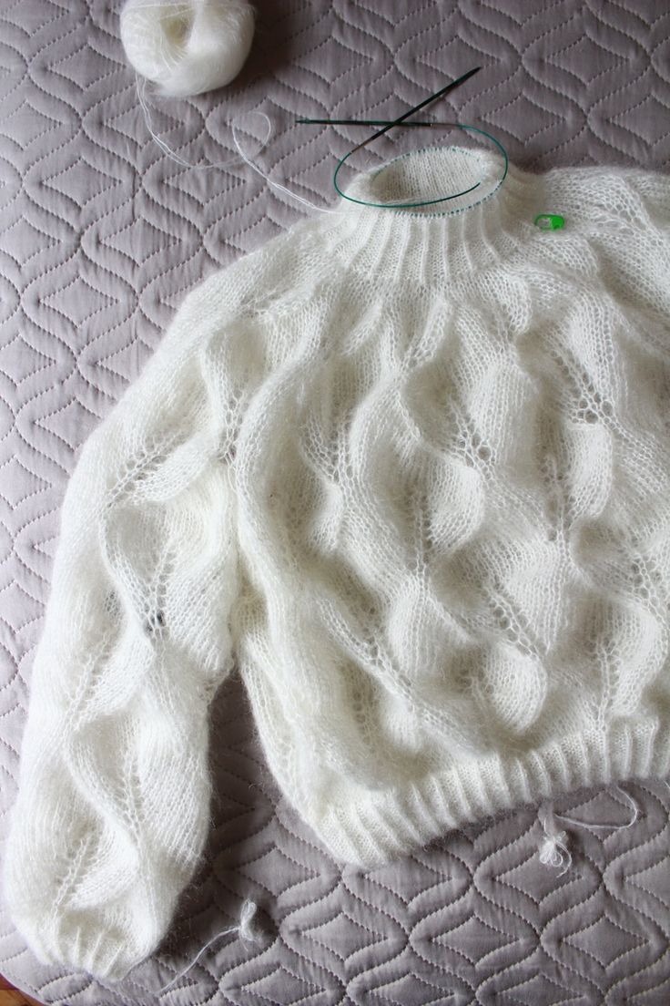 a white knitted sweater sitting on top of a bed next to a ball of yarn