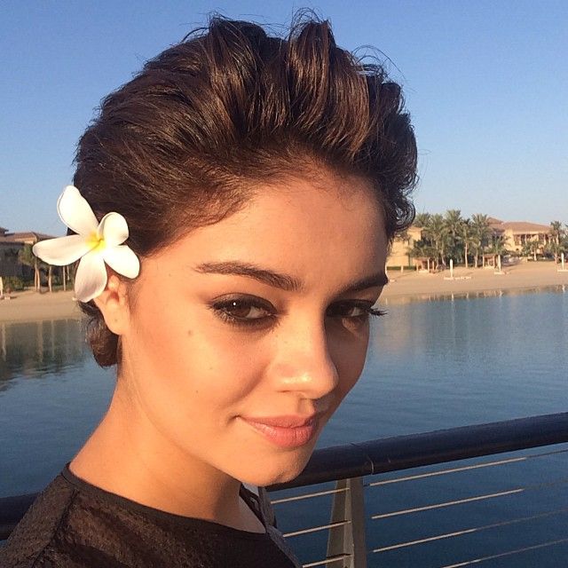 a woman with a flower in her hair standing on a pier near the water and looking at the camera