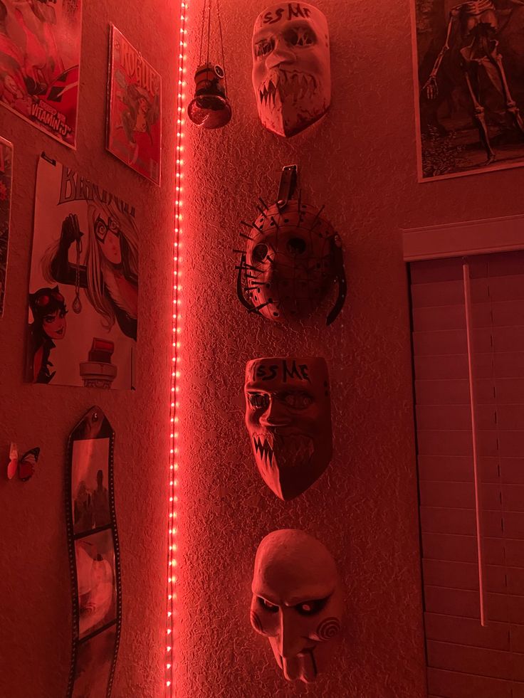 several masks are hanging on the wall with red light coming from behind them in a dark room