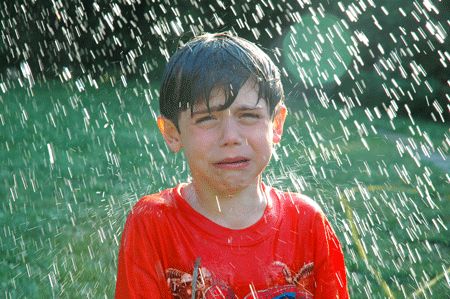 a young boy standing in front of a sprinkled fire hydrant on a sunny day