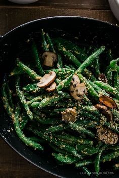 green beans and mushrooms in a skillet on a wooden table next to some sauce