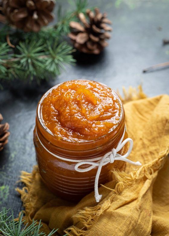 a jar filled with orange marmalade sitting on top of a yellow napkin next to pine cones