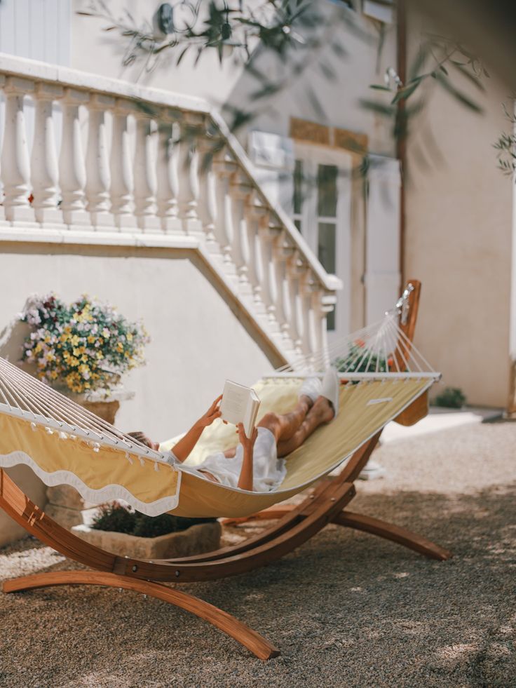 a woman laying in a hammock reading a book on the front steps of a house