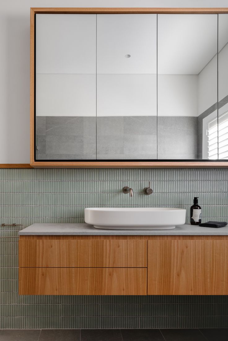 a bathroom with a large mirror above the sink and wooden cabinetry on the wall