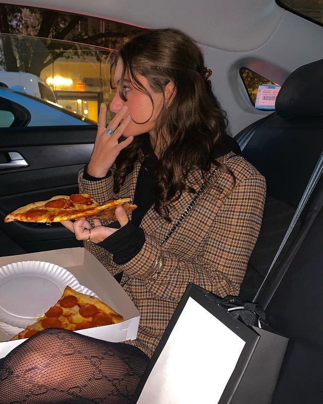 a woman sitting in the back seat of a car eating pizza