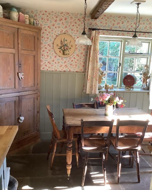 a dining room table and chairs in front of a window with floral wallpaper on the walls