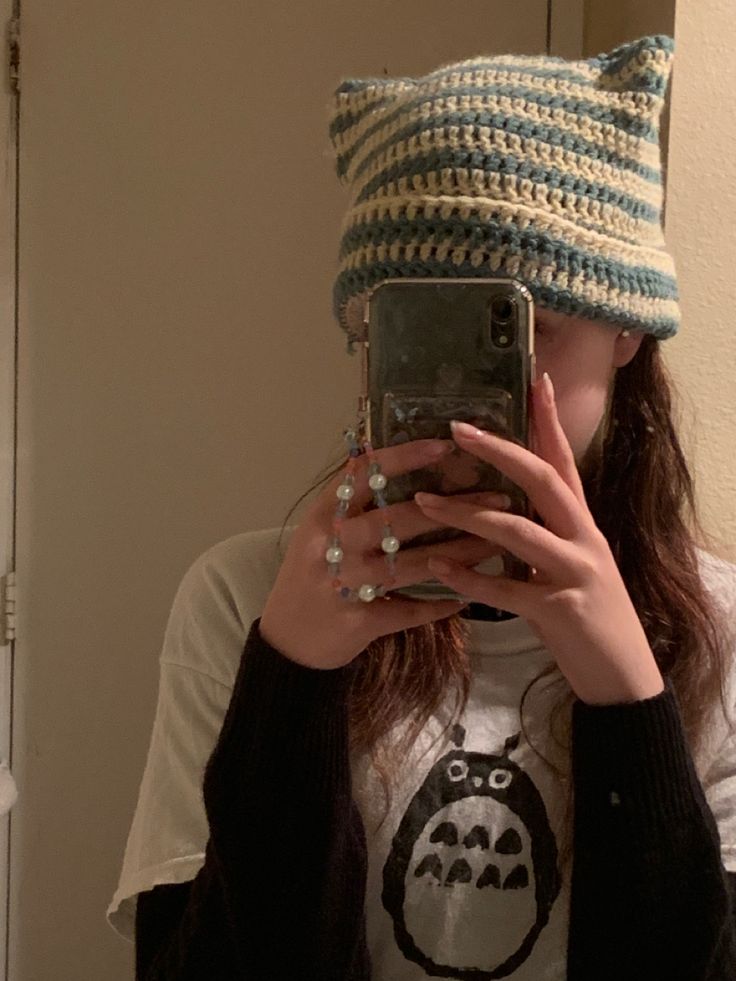 a woman taking a selfie in front of a mirror wearing a knitted cat hat