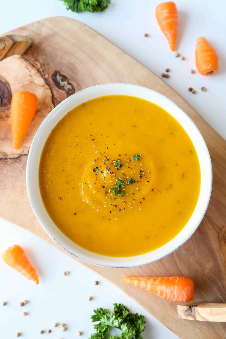 a white bowl filled with carrot soup on top of a wooden cutting board next to some broccoli