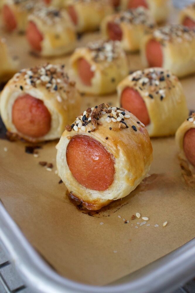 hotdogs wrapped in bread and sprinkled with sesame seeds on a baking sheet