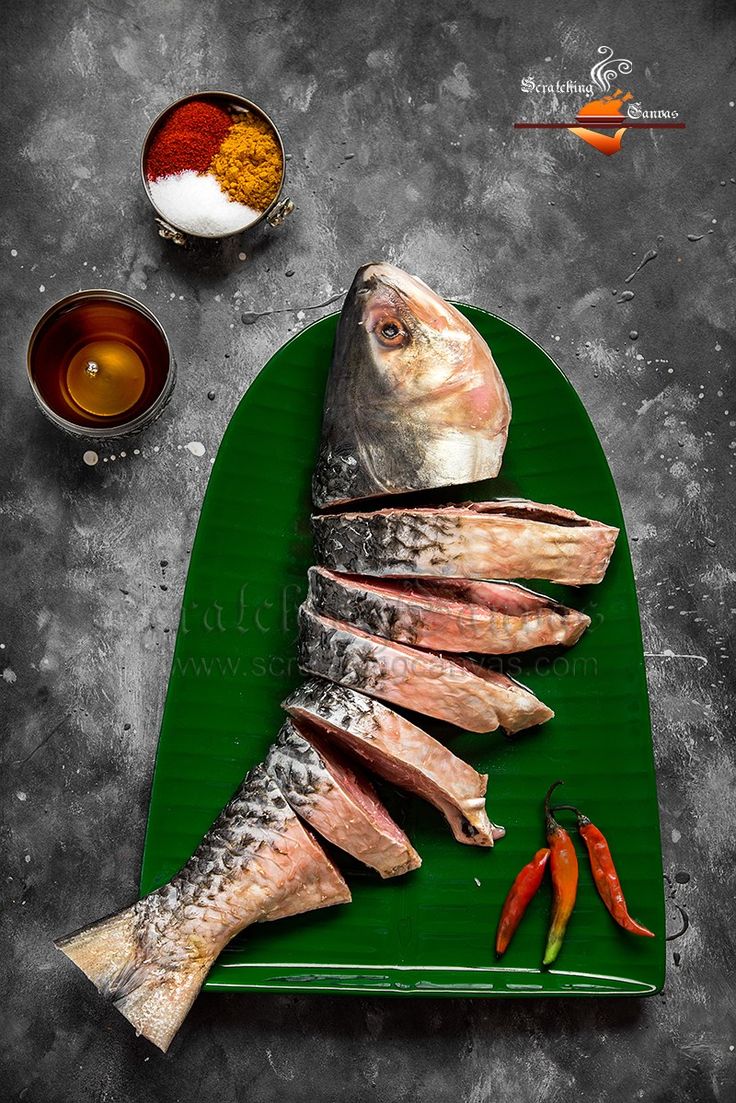 fish on a green platter with spices and seasoning next to it, ready to be cooked