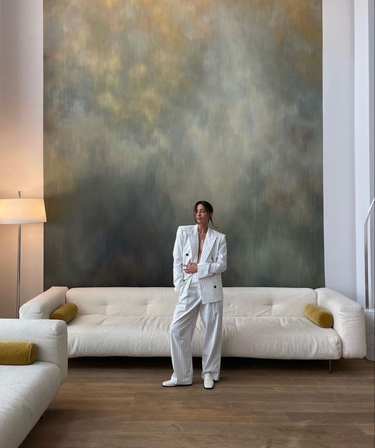 a woman standing in front of a couch with a painting behind her on the wall