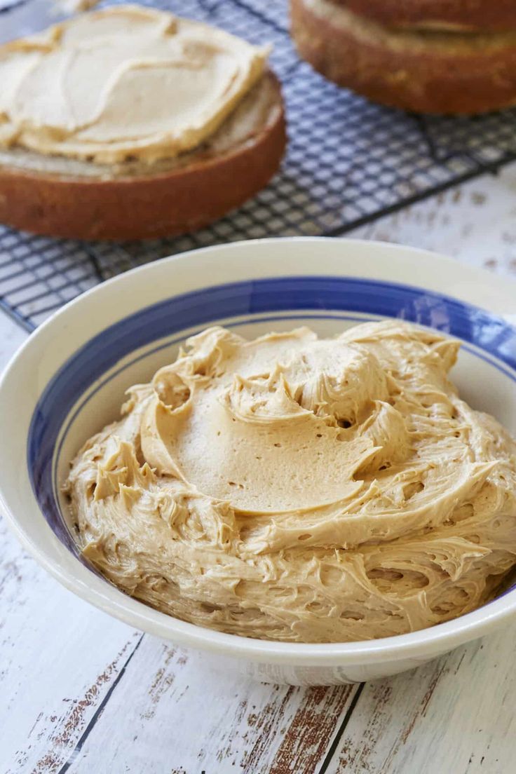 a white bowl filled with peanut butter next to two loaves of bread