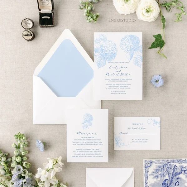 the wedding stationery is laid out with blue and white flowers, cards, and envelopes