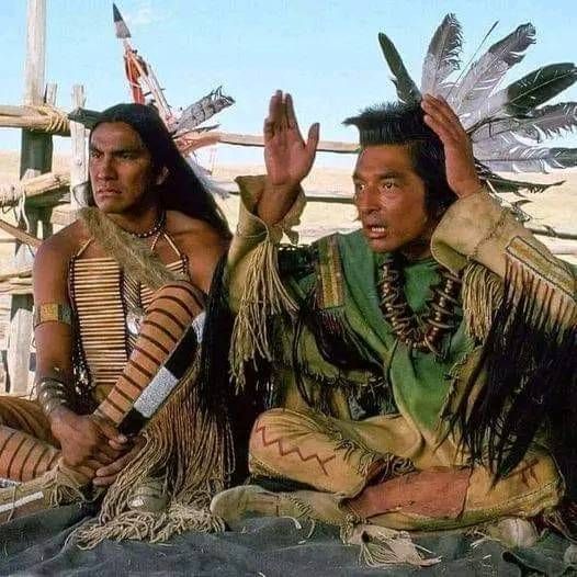 two native american men sitting on the ground with their hands up in front of them