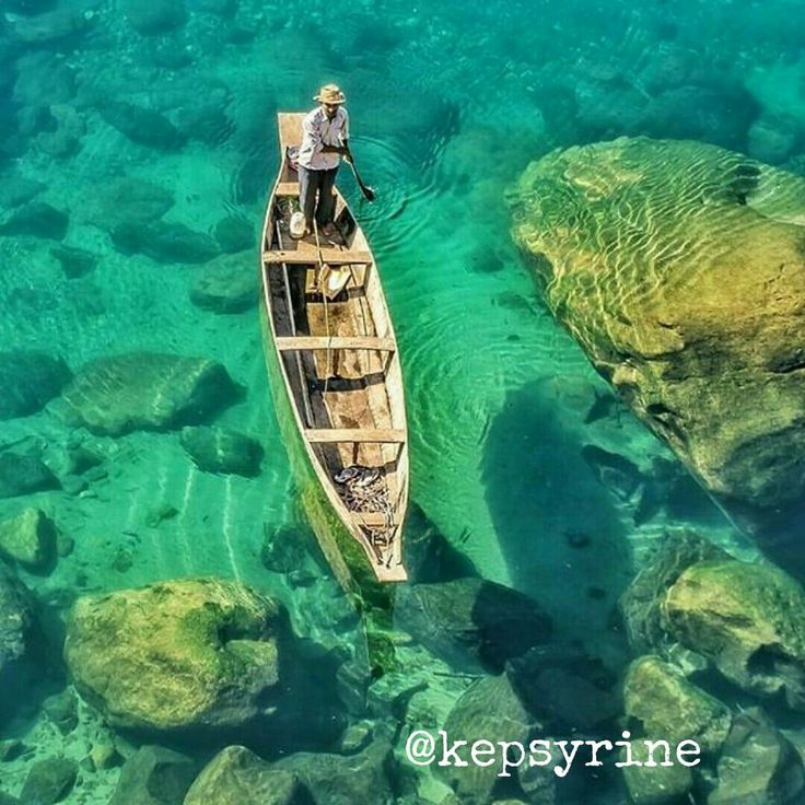 a man in a canoe floating on the water near some rocks and green algaes