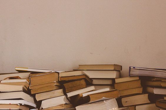 a pile of books sitting on top of a wooden table next to a white wall