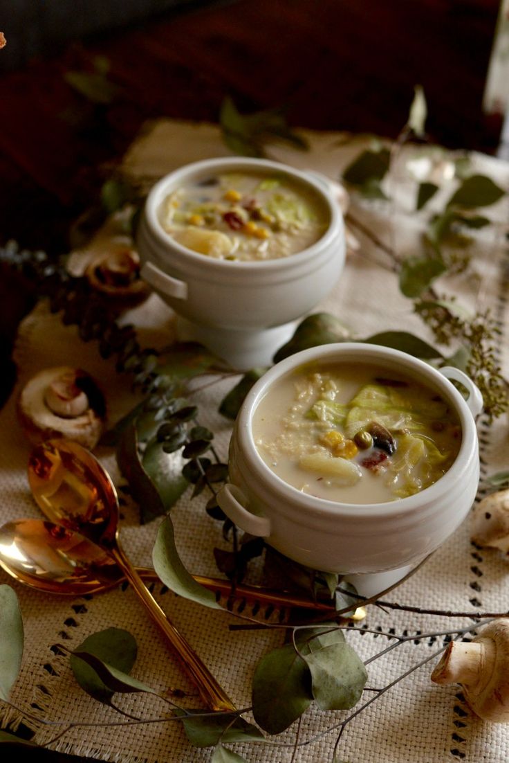 two white bowls filled with soup sitting on top of a table next to spoons