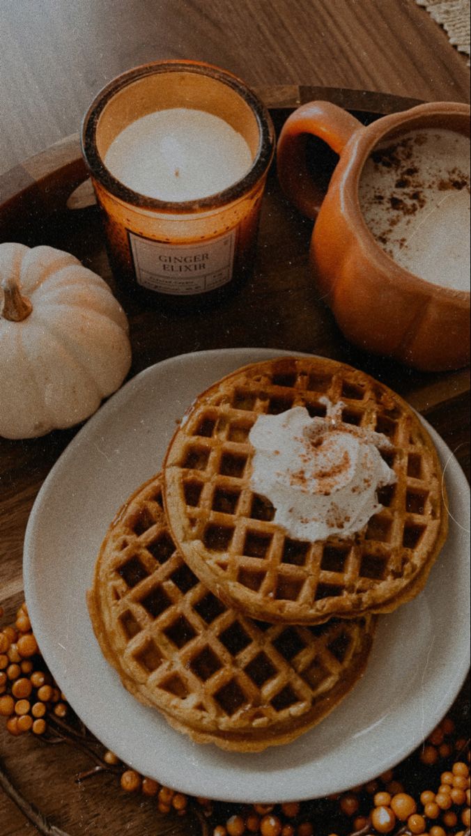 three waffles on a white plate next to two cups of coffee and pumpkins