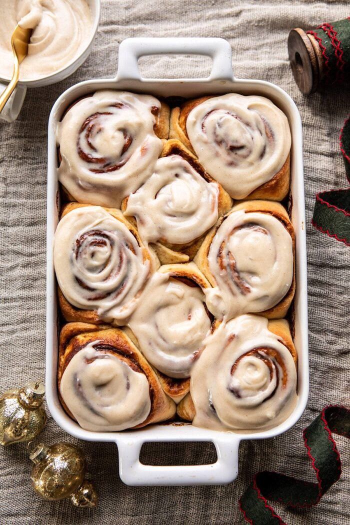 cinnamon rolls with cream cheese frosting in a white baking dish next to christmas decorations