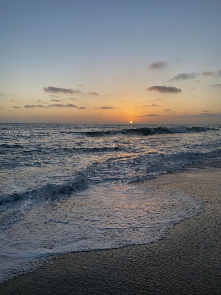 the sun is setting over the ocean with waves coming in to shore and some clouds