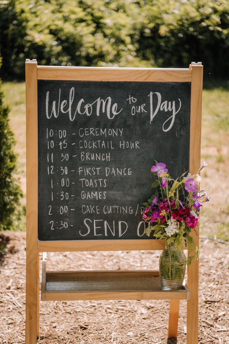 a welcome sign with flowers in a vase sitting on a wooden bench next to it