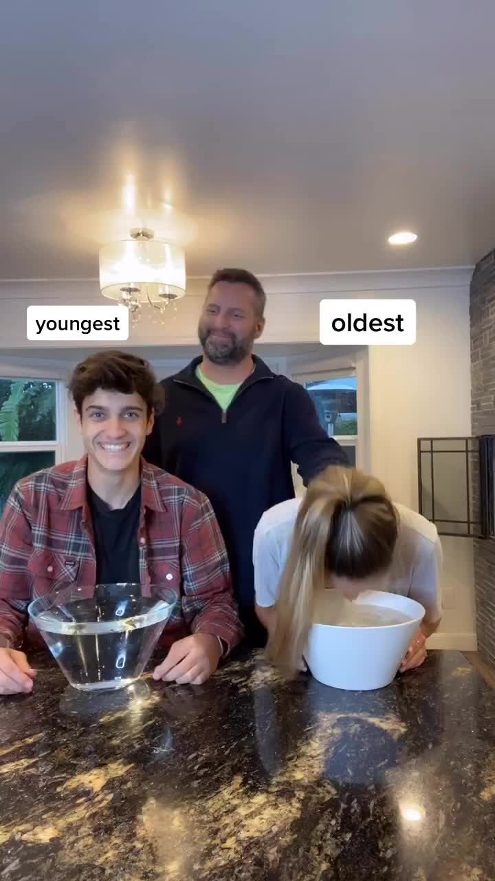 two men standing behind a counter with a bowl on it and another man holding a hair dryer in front of them