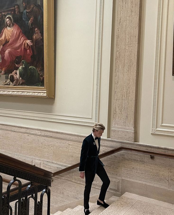 a man in a suit walking down some stairs with a painting on the wall behind him