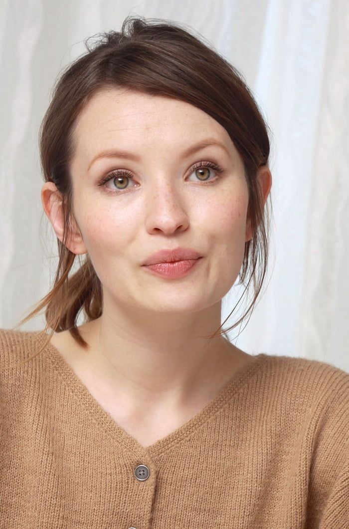 a woman is posing for the camera with her hair in a pony tail and wearing a brown sweater