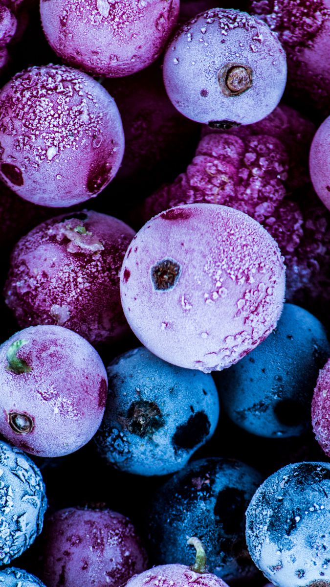 some blueberries are covered in pink and purple powdered sugar, with green leaves on the side