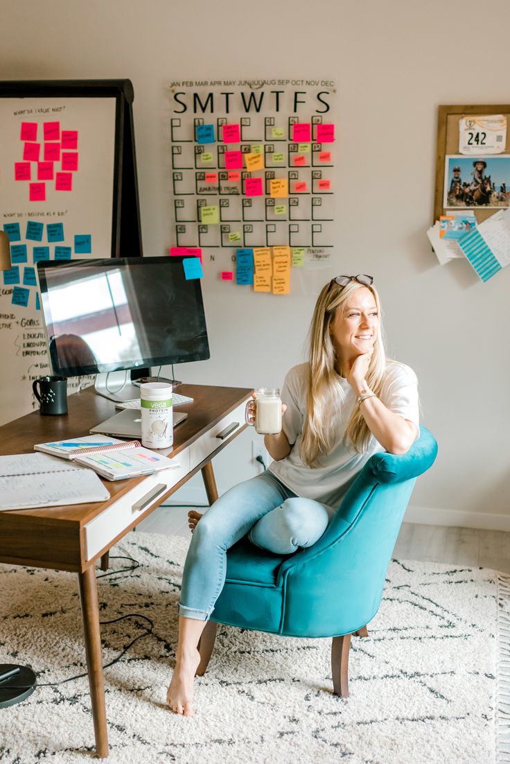 a woman sitting on a blue chair in front of a desk with a computer monitor