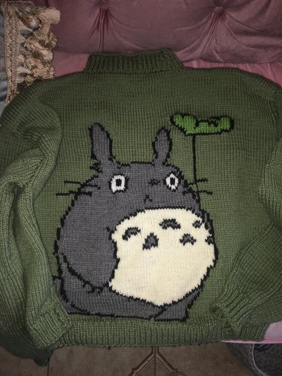 a green sweater with a totoro drawn on the front and back, sitting on top of a chair