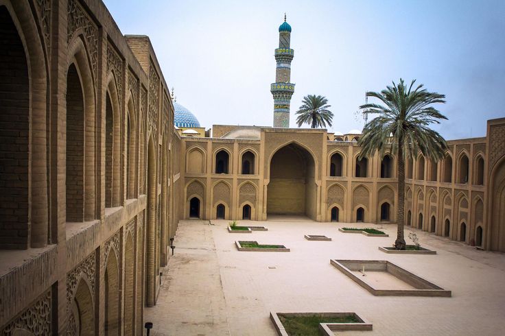 the courtyard of an old building with palm trees in the foreground and a tall tower behind it