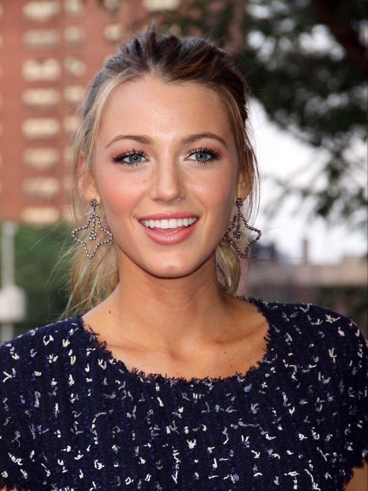 a woman with blonde hair and blue eyes smiles at the camera while wearing large earrings